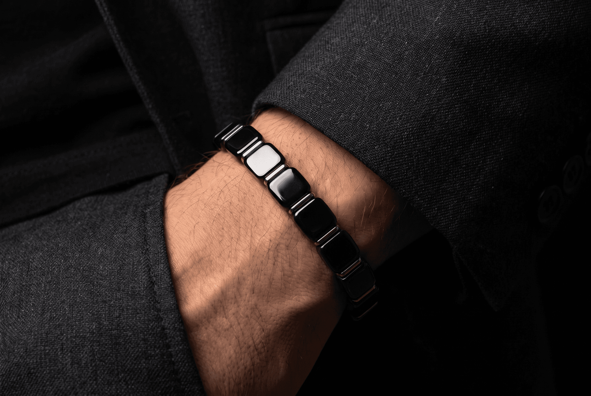 Editorial photograph of a man's wrist wearing a black beaded bracelet with a dark suit cuff