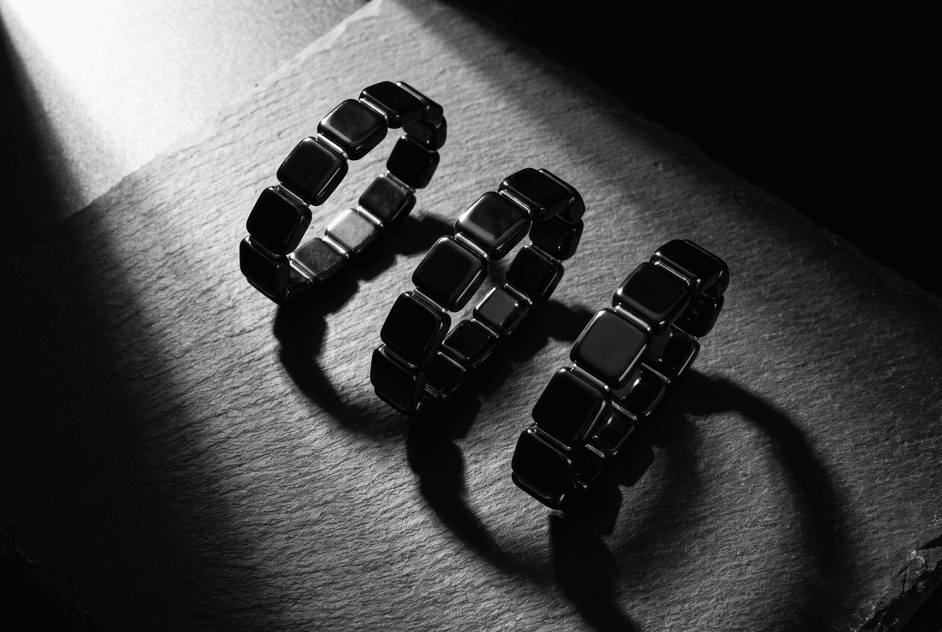 Flat lay photograph of three black beaded bracelets arranged on a dark slate surface