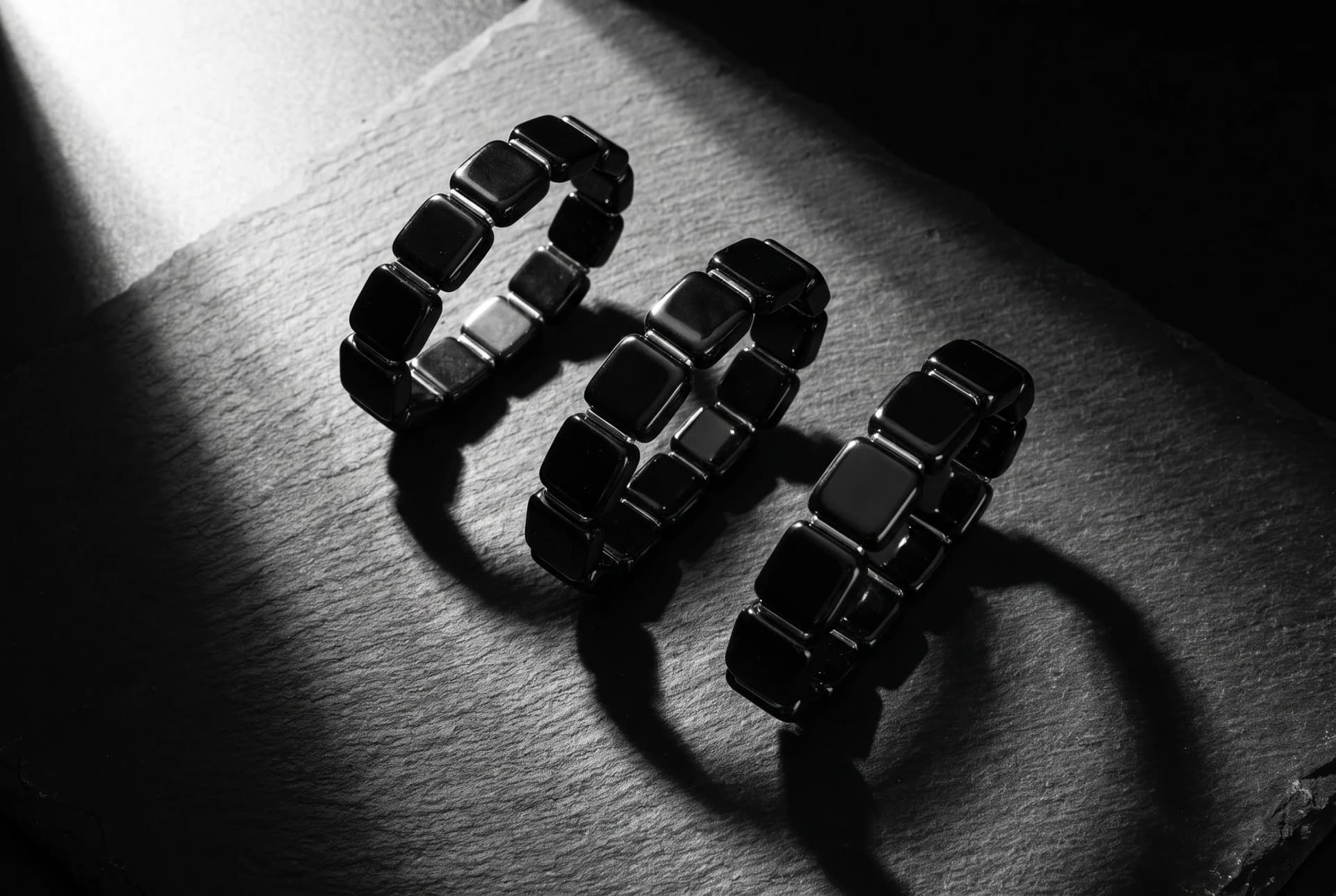 Flat lay photograph of three metallic hematite beaded bracelets arranged on a dark slate surface