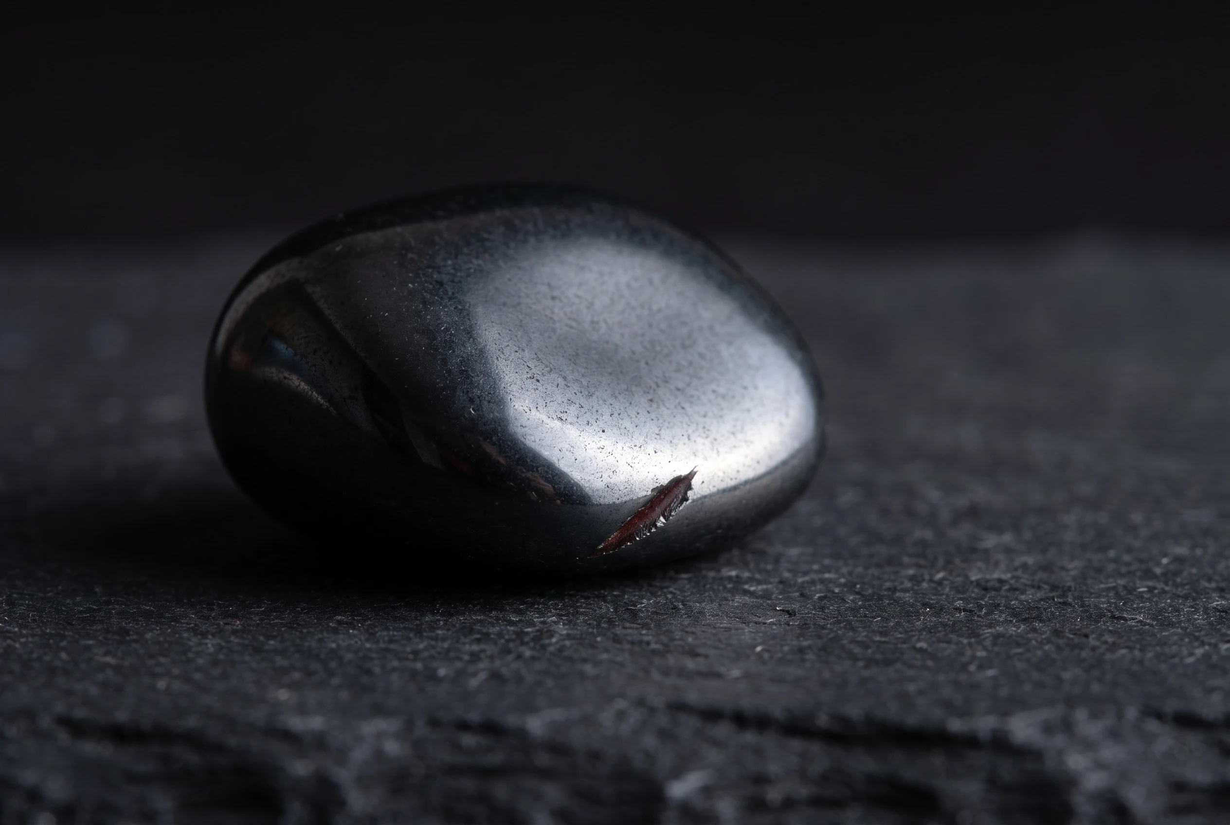 Macro photograph of a polished hematite stone with a small scratch revealing its red-brown iron oxide streak under dramatic side lighting