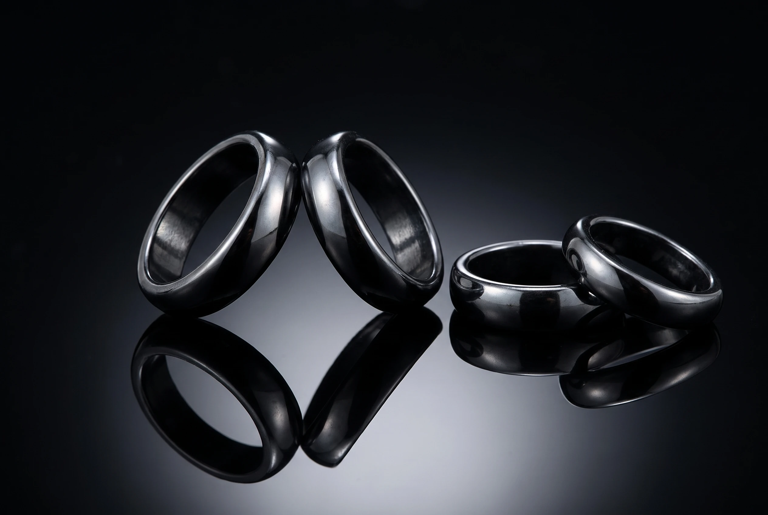 Macro studio photograph of two pairs of Curved Hematite Rings tilted toward each other on a dark reflective surface