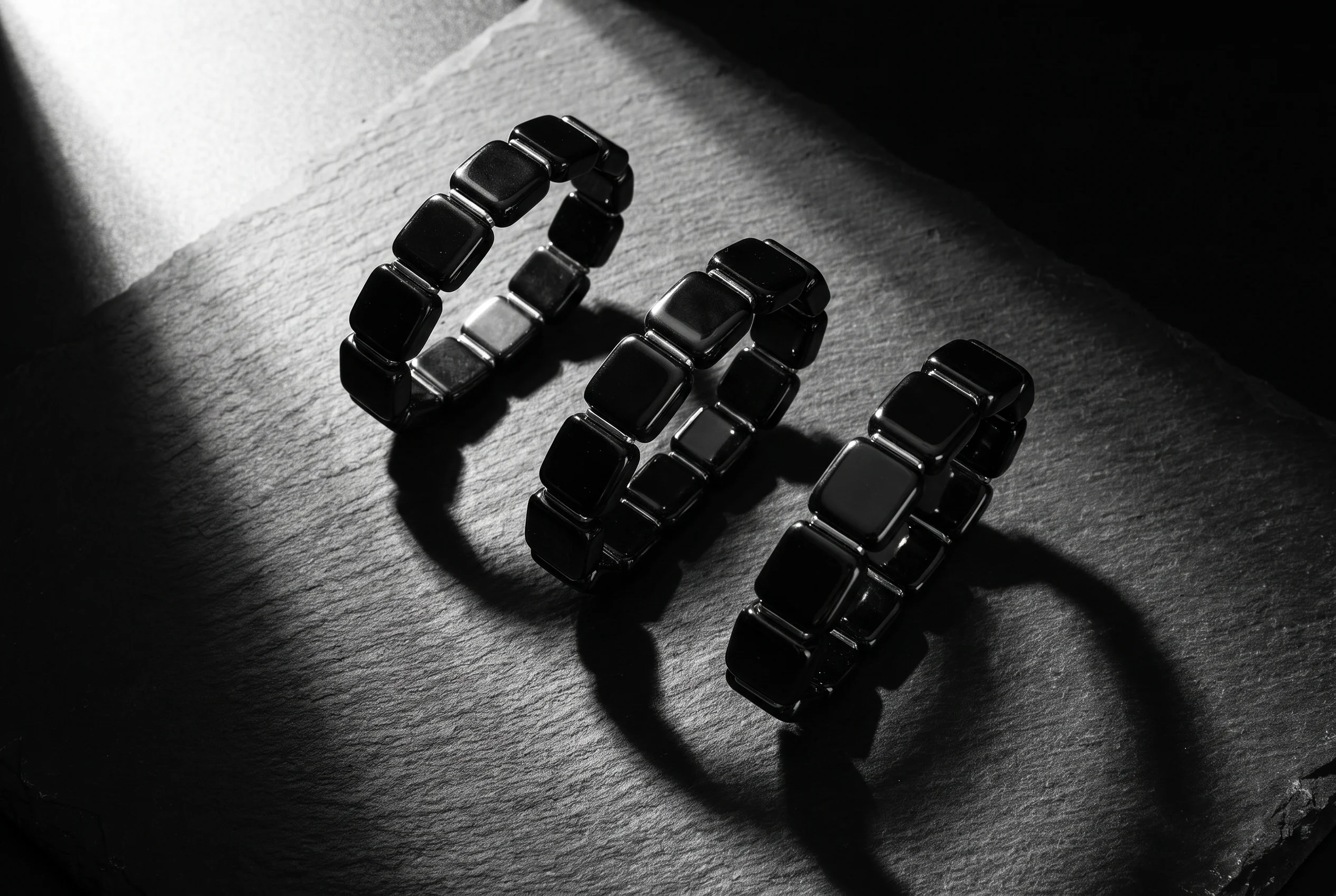 Flat lay photograph of three metallic hematite beaded bracelets arranged on a dark slate surface